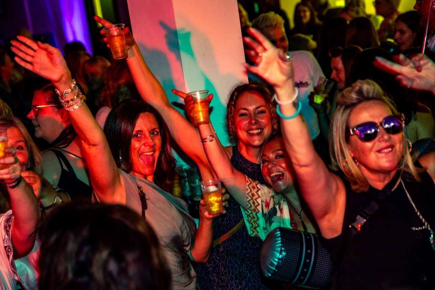 Women singing with arms up under coloured lights