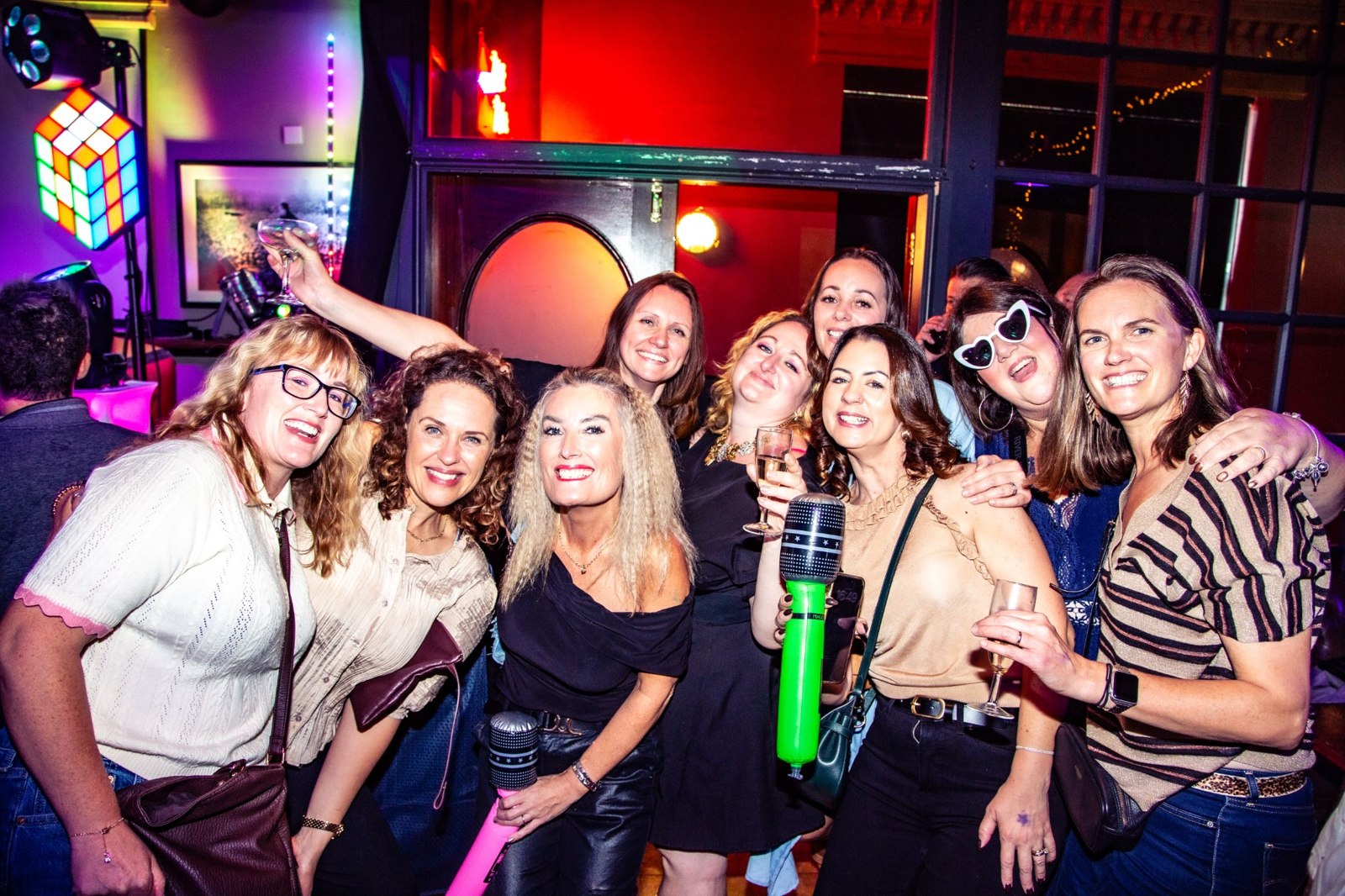 A large group of friends smiling together with colourful inflatable microphones